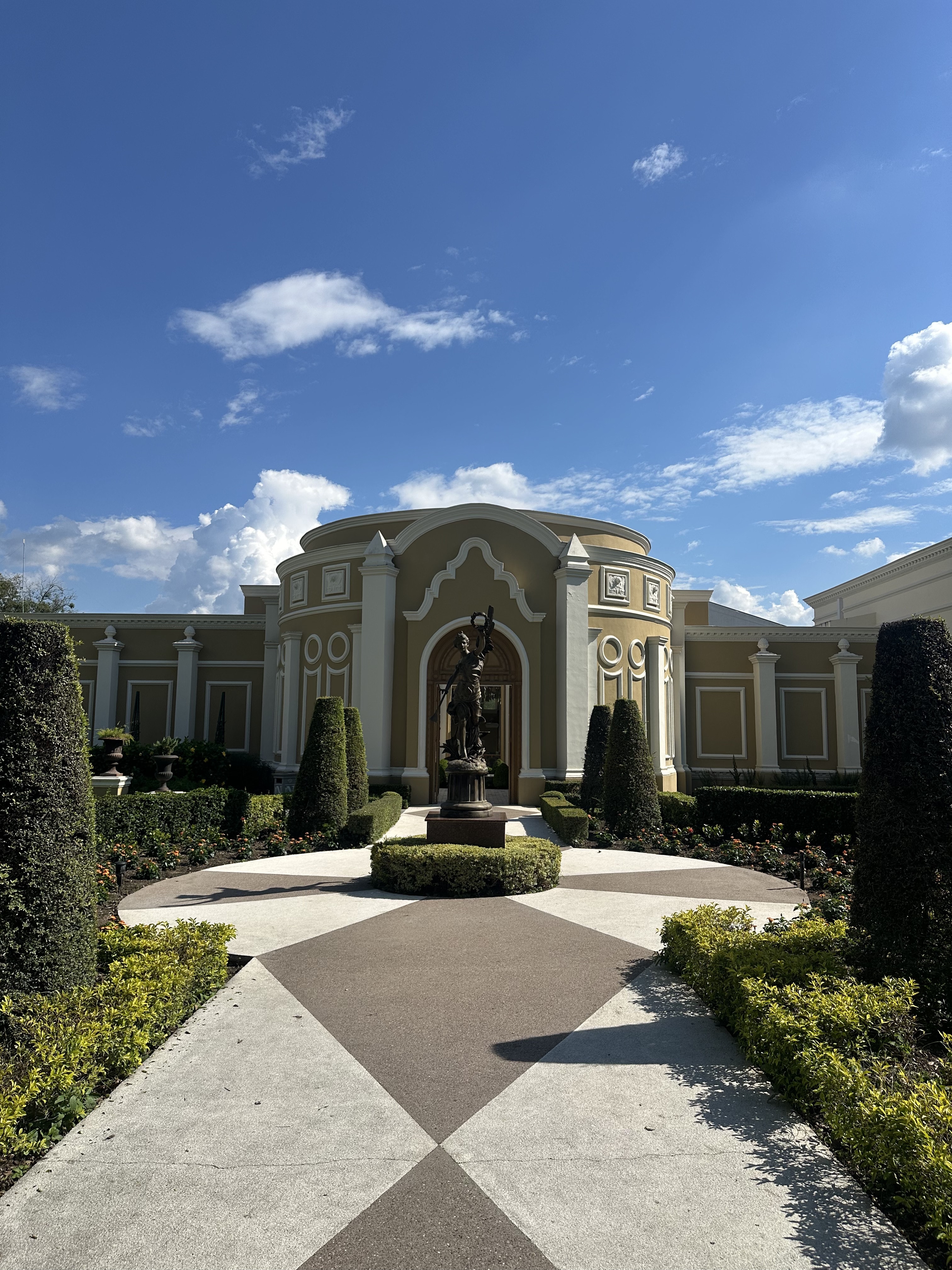 The entrance of Las Nubes Eventos: a bronze statue in a formal garden before an arched doorway